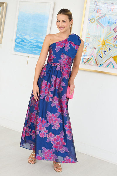 Woman wearing a blue floral one-shoulder dress in an art gallery setting.